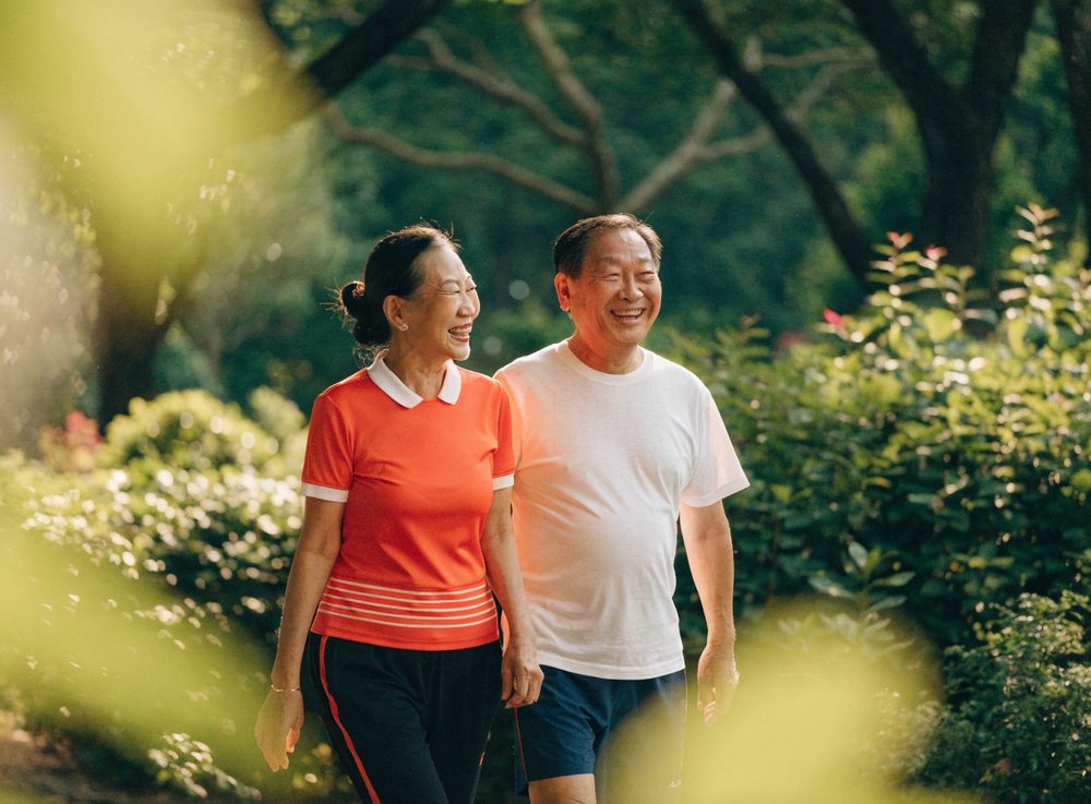 A smiling Singaporean couple walking together in a park, staying active as they age