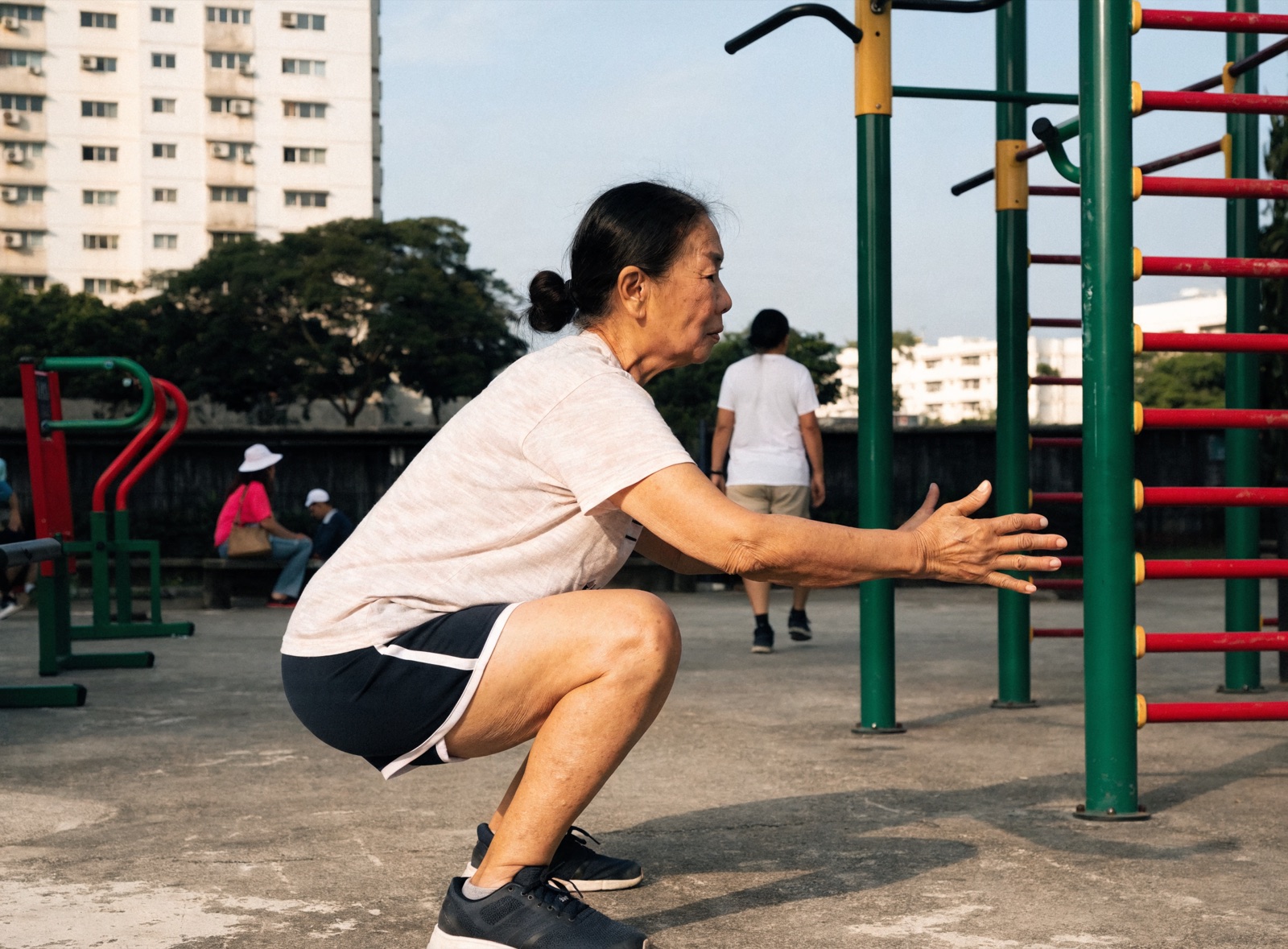 An older woman doing a bodyweight squat with good form at an outdoor fitness corner in Singapore